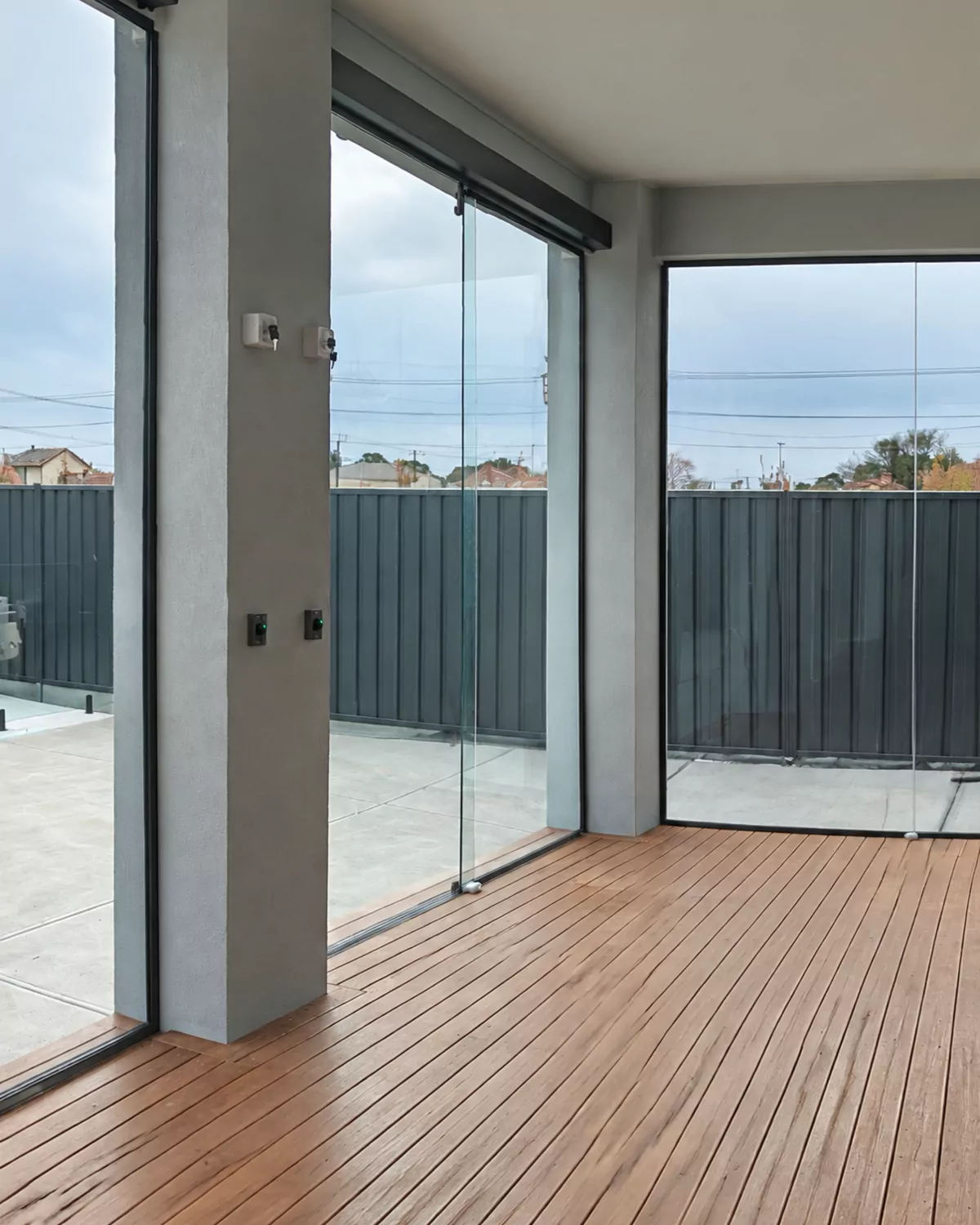 Inside an enclosed alfresco on a grey day, with one frameless glass panel slid partly open between rendered columns