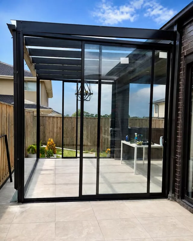 The finished glass room: black-framed sliding glass walls and a glass roof over a tiled floor