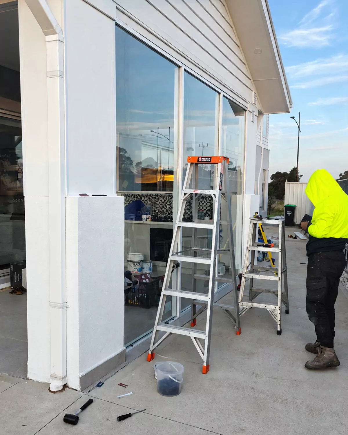 An installer in a high-visibility jacket beside ladders and newly fitted glass panels on the alfresco