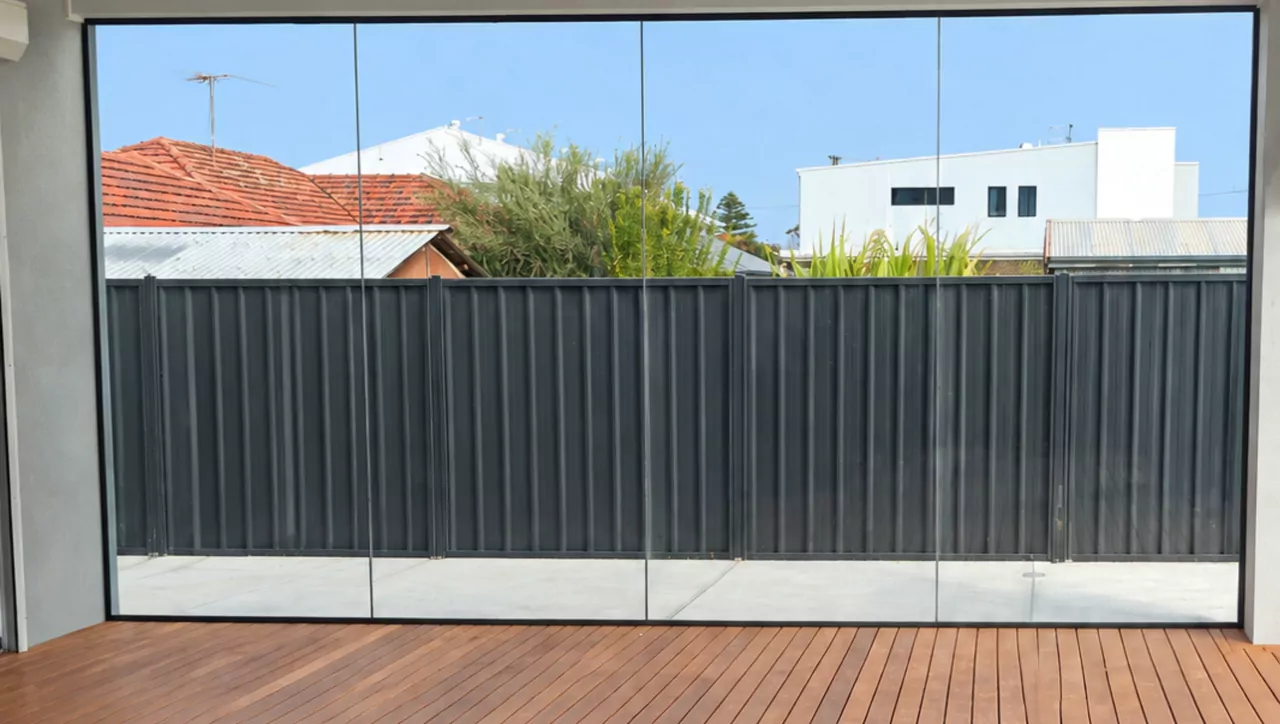 Looking out from an enclosed alfresco through a wall of frameless sliding glass panels, with a timber deck in the foreground
