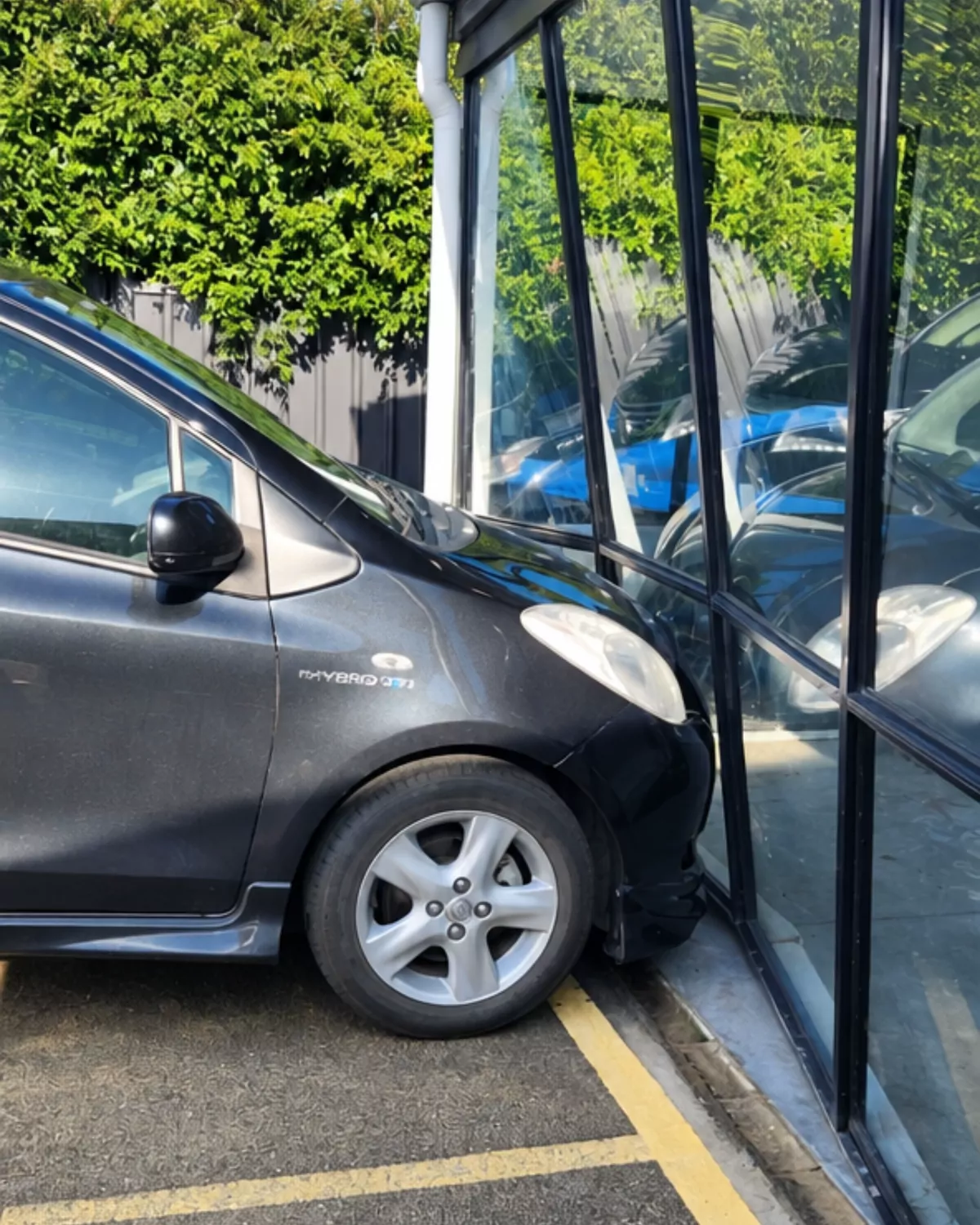 Before: a car pushed into a black-framed glass wall, the frame bent and the glass broken