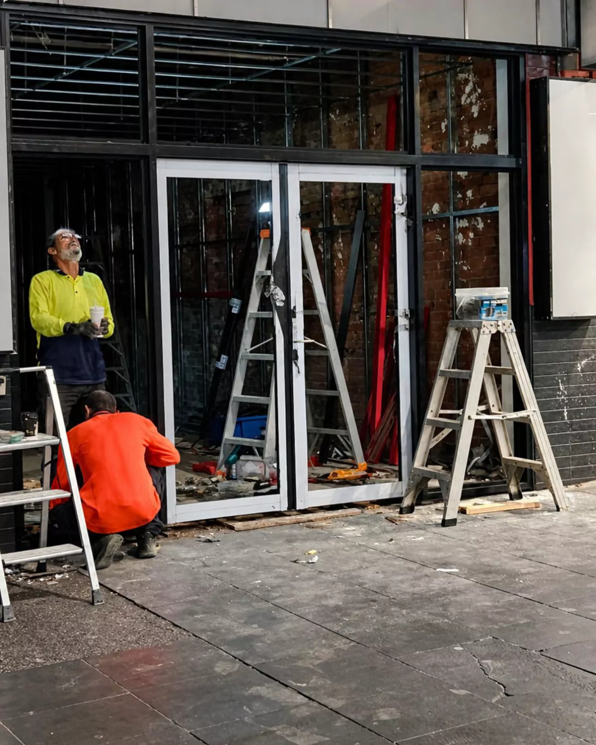 Two Glassy Slide installers fitting a new black frame and white double doors to the shopfront