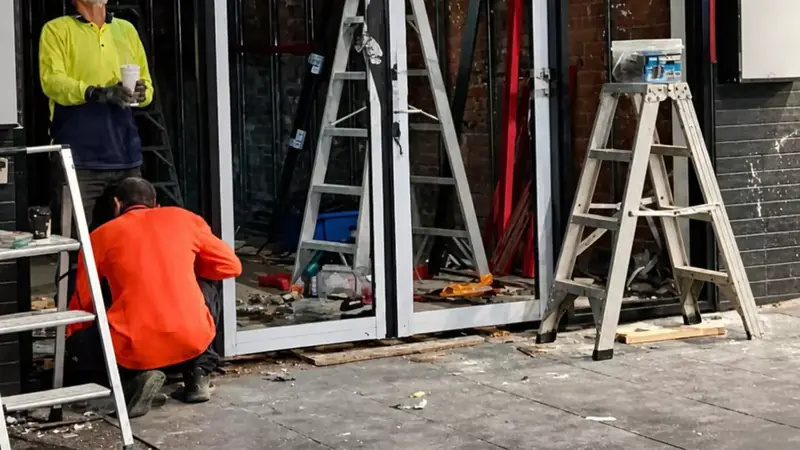 Two glaziers fitting new aluminium-framed glass doors into a city shopfront.