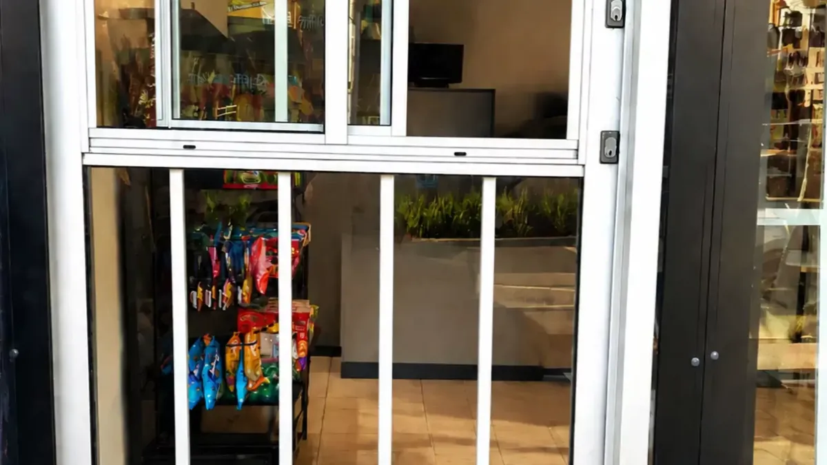 A white aluminium shop entry door with security bars, fitted in daylight.