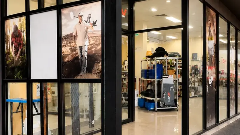 A black aluminium-framed shopfront with glass panels and a glass entry in a shopping strip.